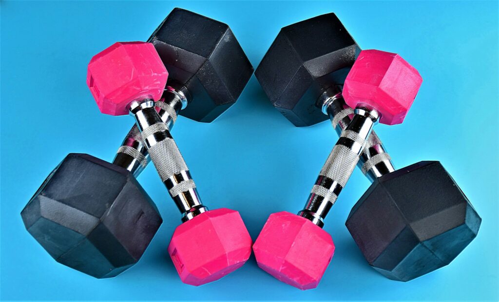 Set van verstelbare dumbbells met roze en zwarte gewichten voor krachttraining thuis, op een blauwe achtergrond